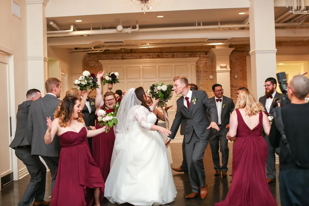 Newlyweds dance with guests in red dresses around them.