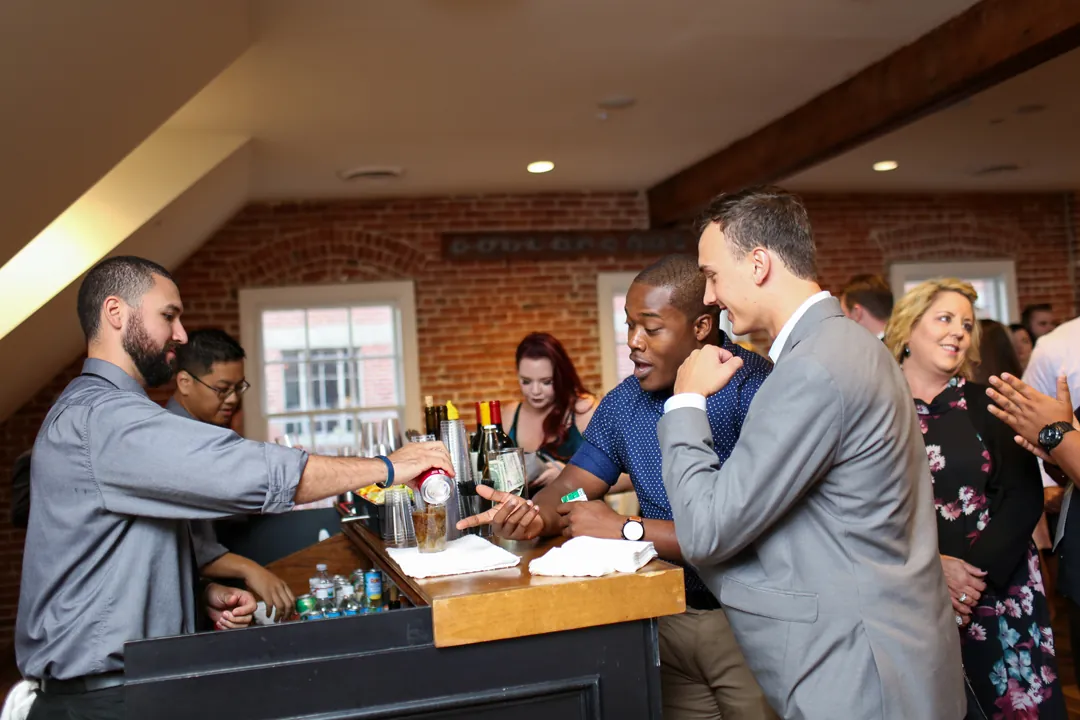Wedding guests raise drinks around an indoor bar.