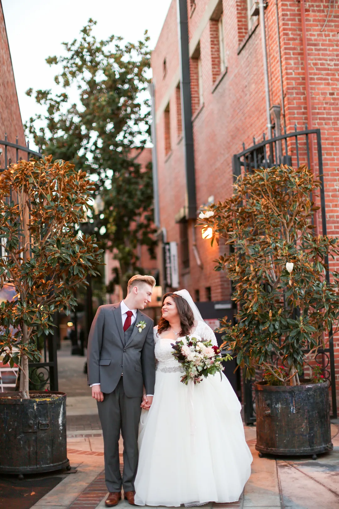 Newlyweds pose beside a tall brick building.