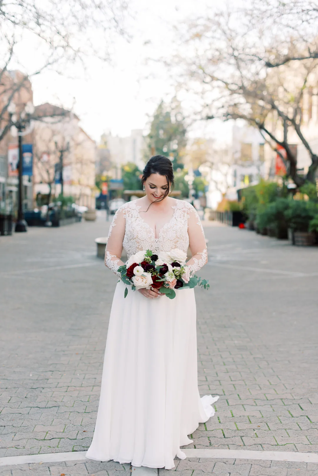 Bride holding a bouquet on a tree-lined city street