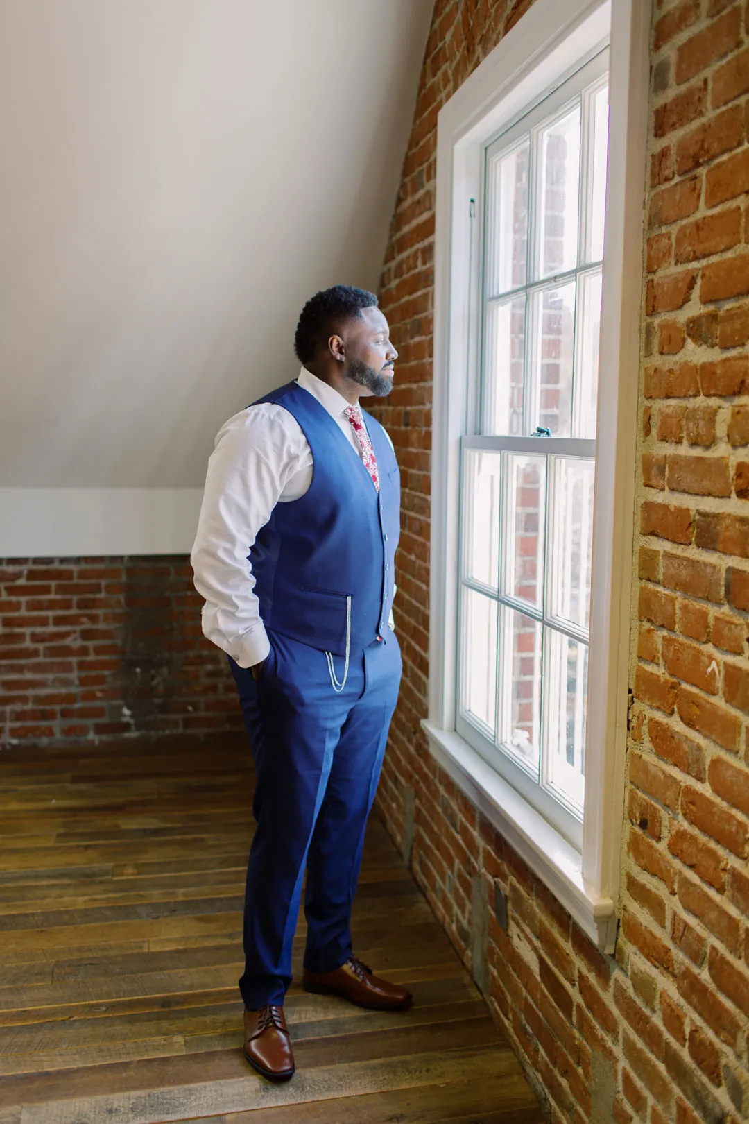 Groom in a blue suit standing beside a tall window