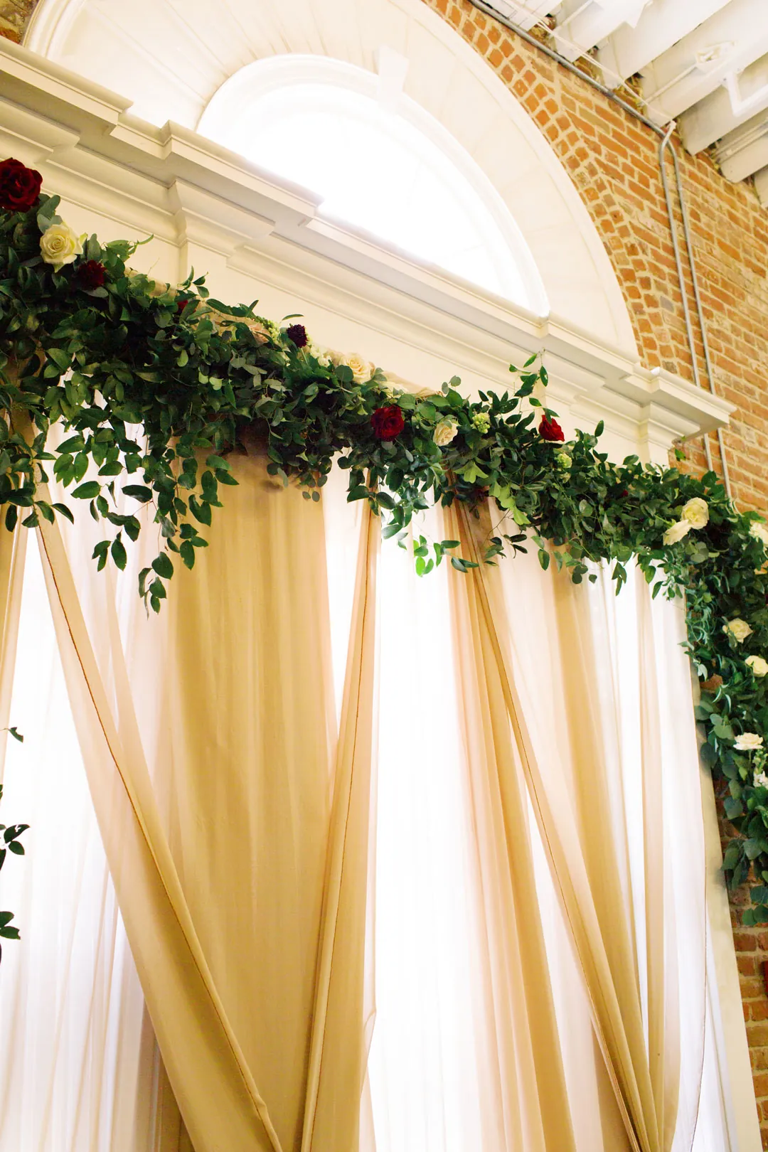 Greenery and flowers decorating a draped ceremony backdrop