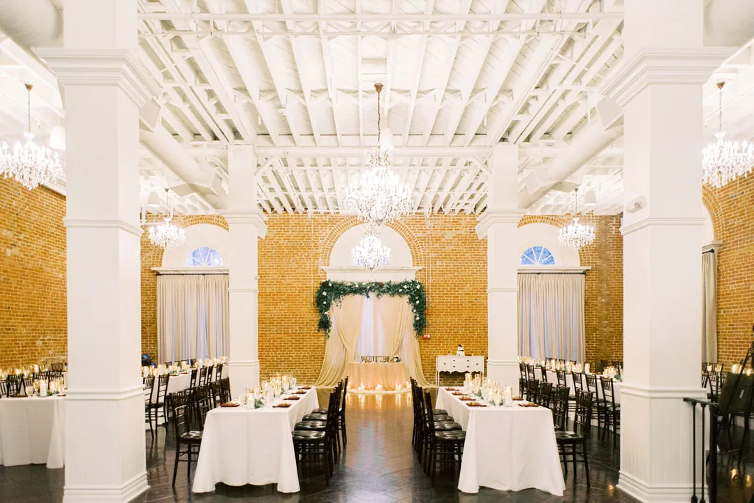 Reception tables beneath chandeliers and a white beamed ceiling