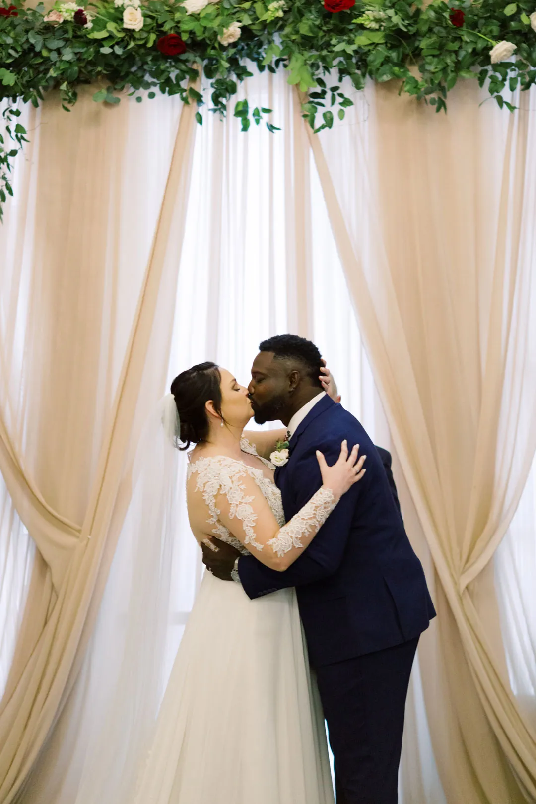 Couple kissing in front of a draped floral backdrop