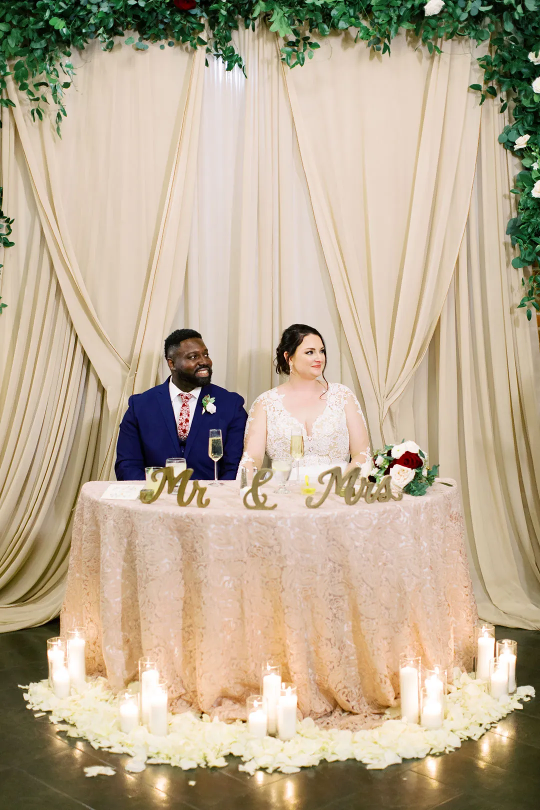 Couple seated at a sweetheart table before pale drapes