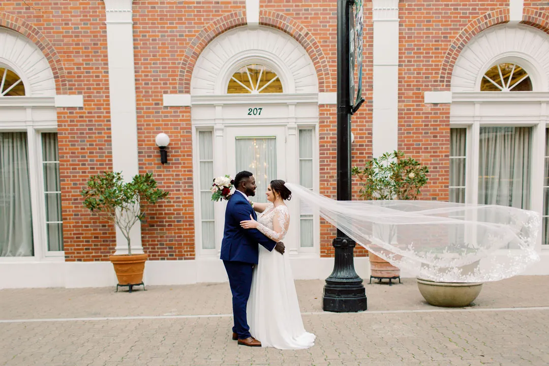 Couple embracing outside a brick building with the veil outstretched