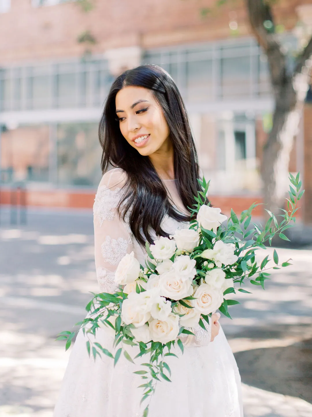 Bride holding a white and green bouquet on a sunny street