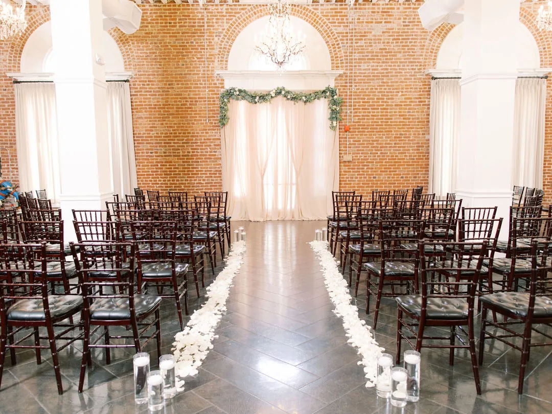 Ceremony aisle lined with white flowers beneath an arched window