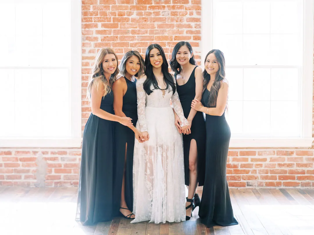 Bride and bridesmaids standing together in front of bright windows