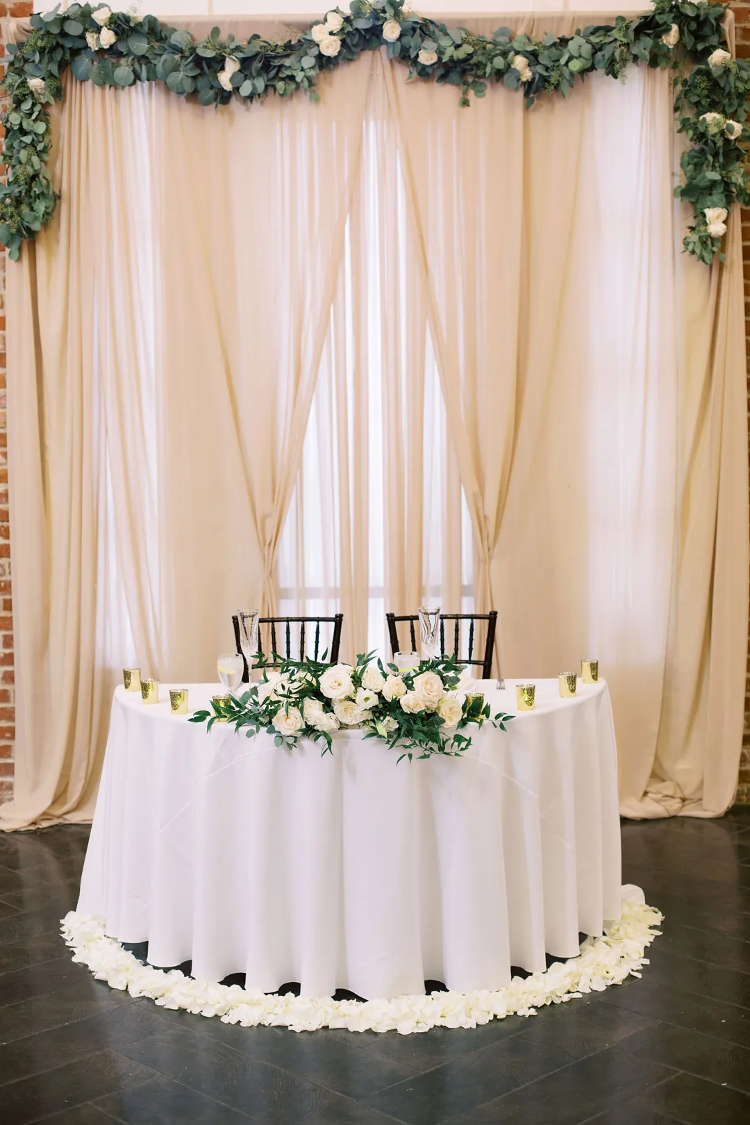 Round sweetheart table beneath pale drapes and greenery