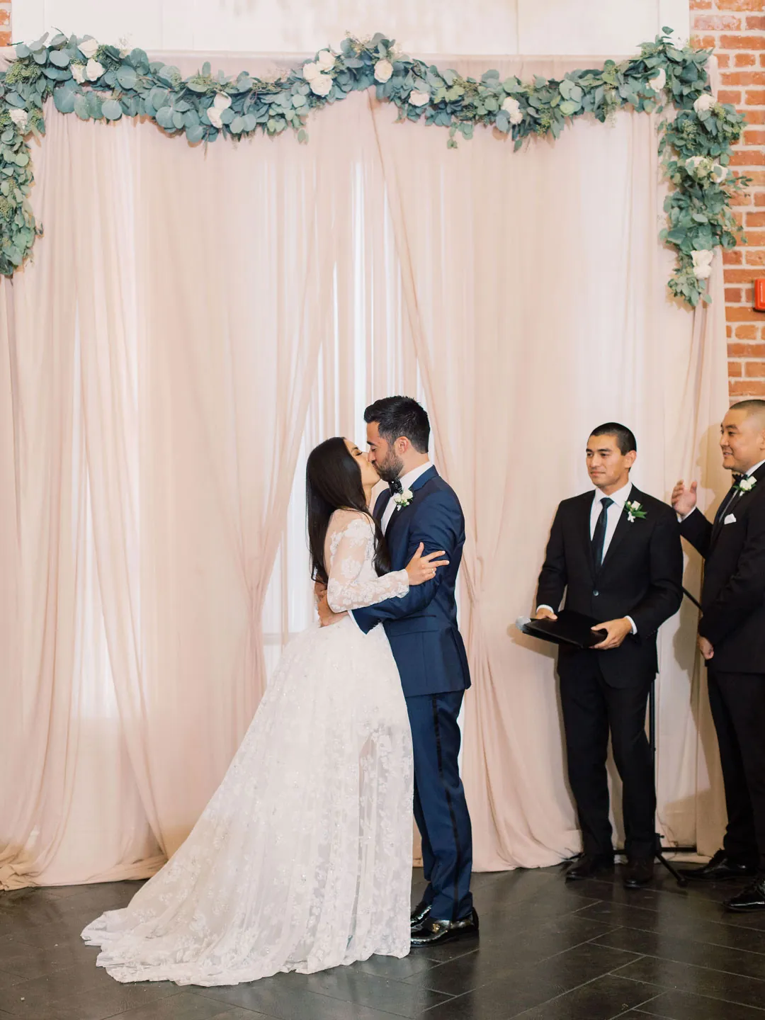 Couple kissing in front of pale ceremony drapes