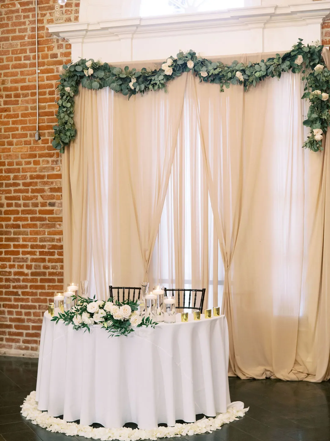 Flower-lined sweetheart table before pale drapes