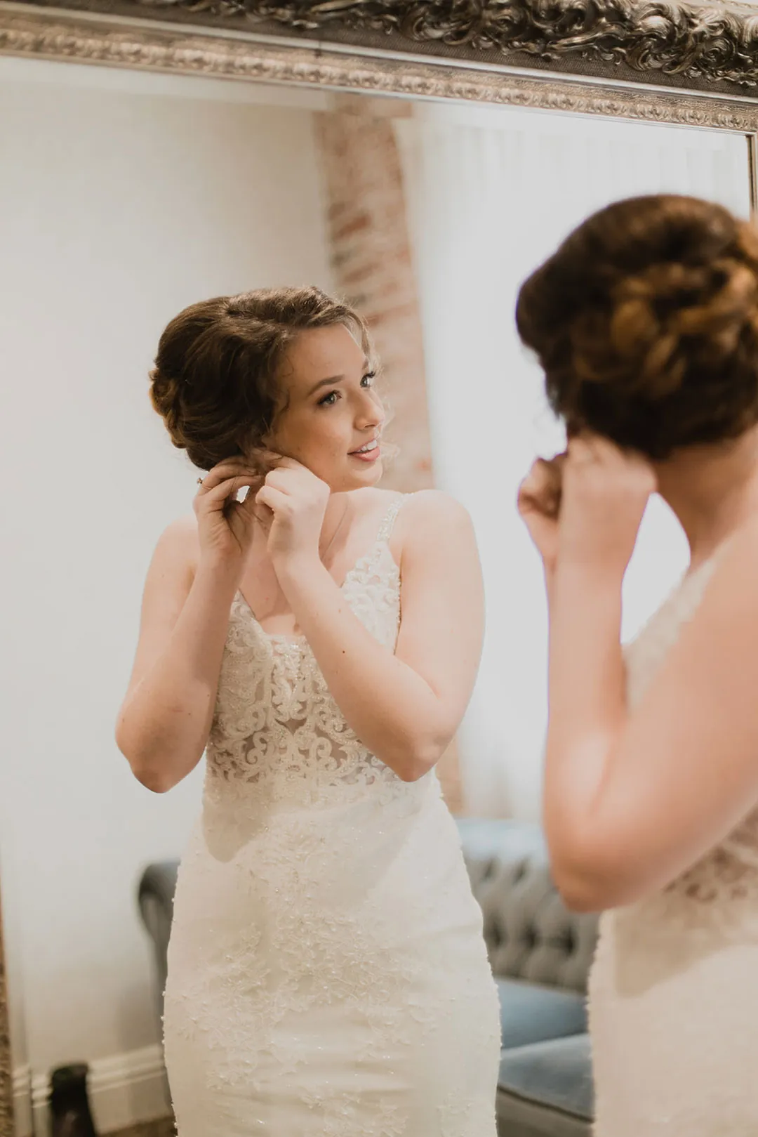 Bride adjusting her earring while looking in a mirror