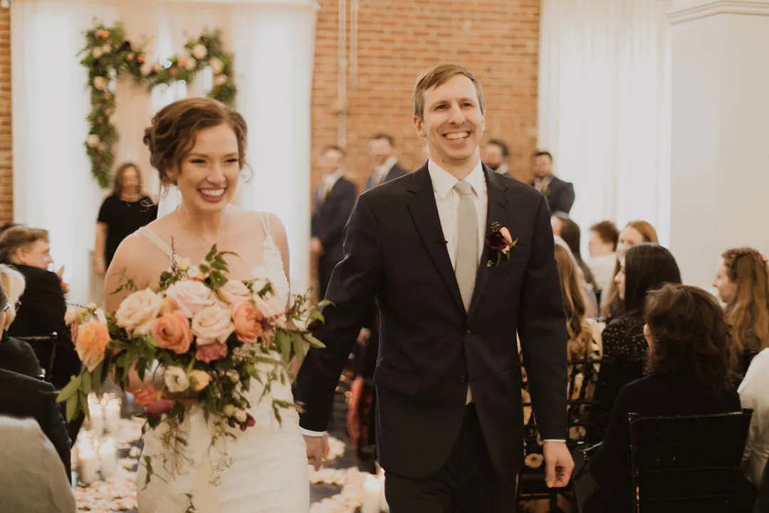 Newlyweds smiling as they walk down the aisle