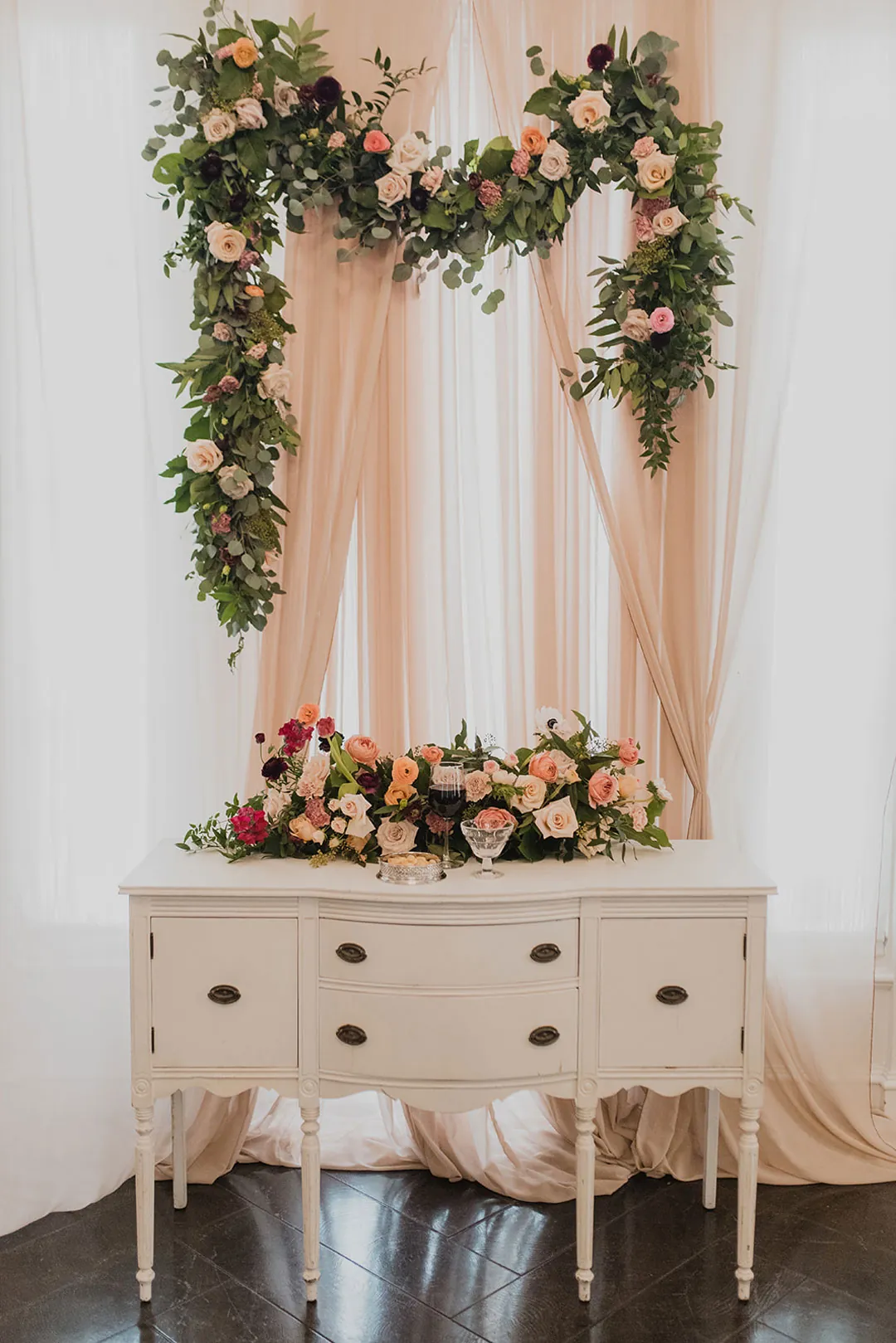 Floral ceremony backdrop above a vintage white dresser