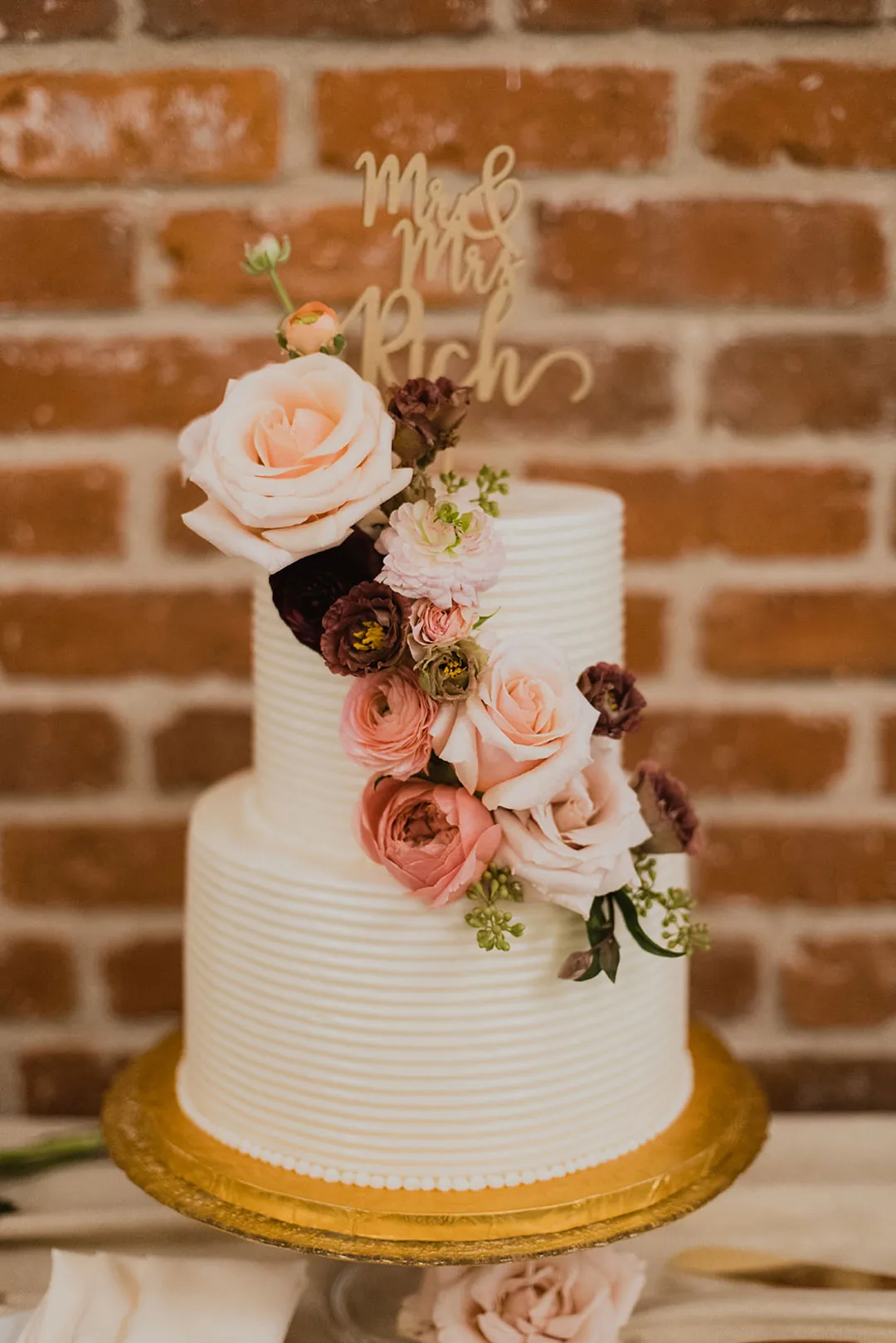 White wedding cake with pink roses and a gold topper