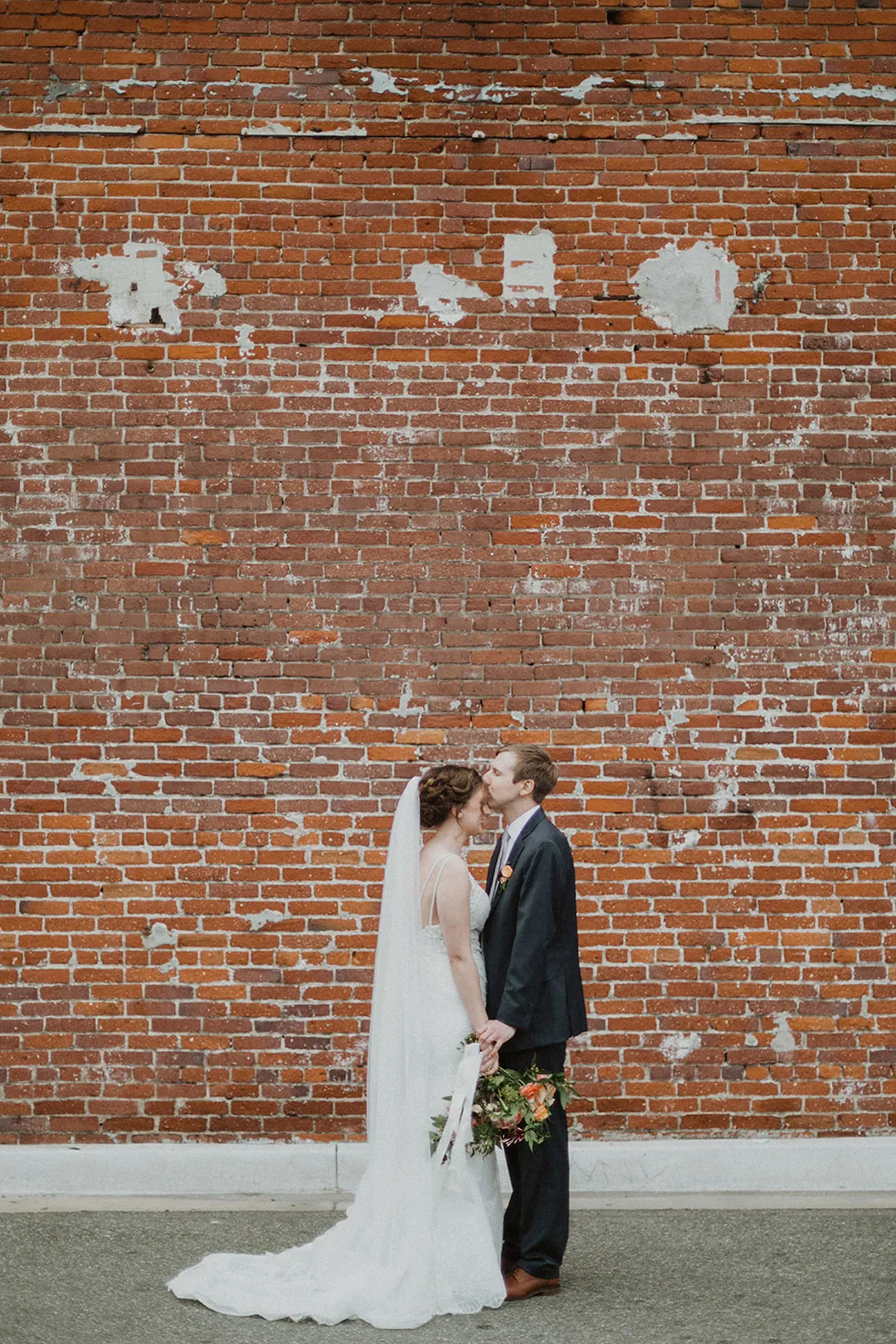 Couple embracing against a large brick wall