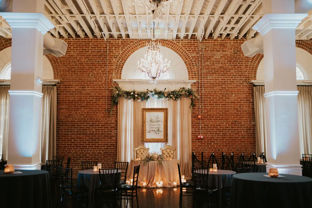 Reception tables in the brick ballroom beneath a chandelier