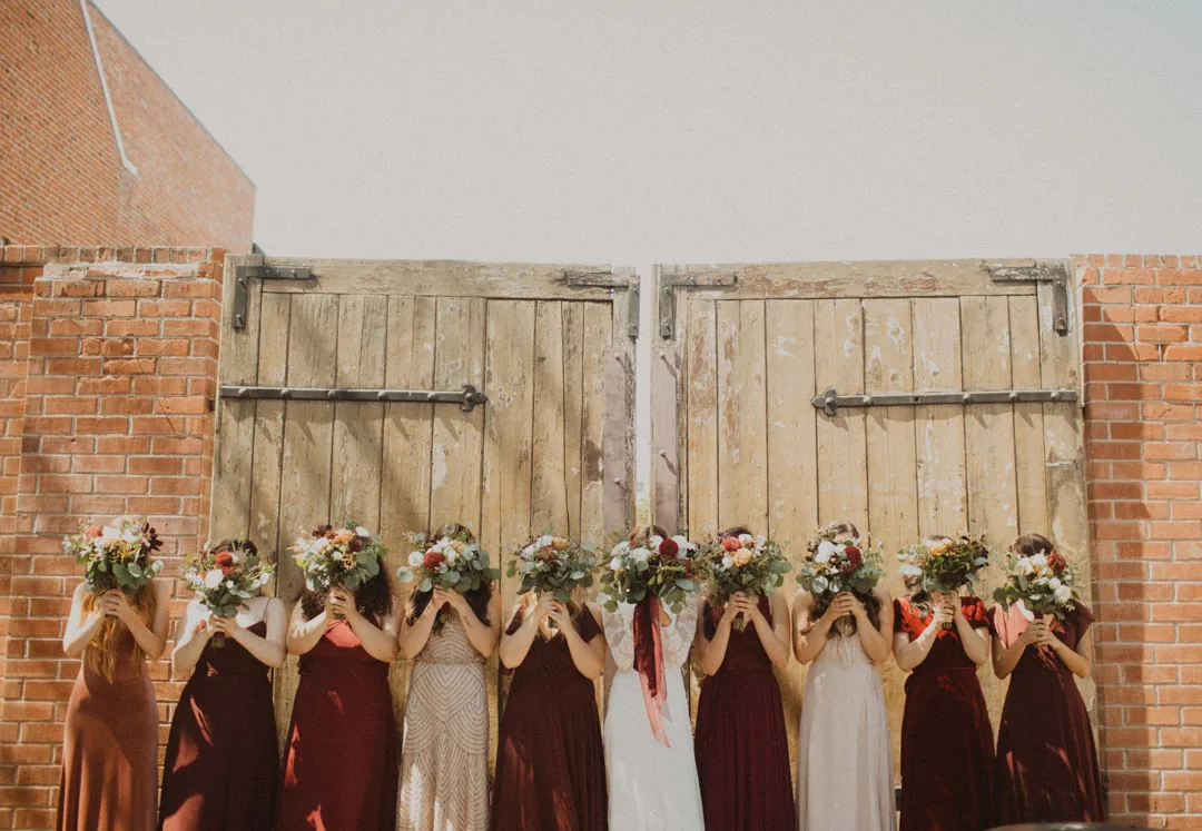 Bridesmaids holding bouquets before wooden doors