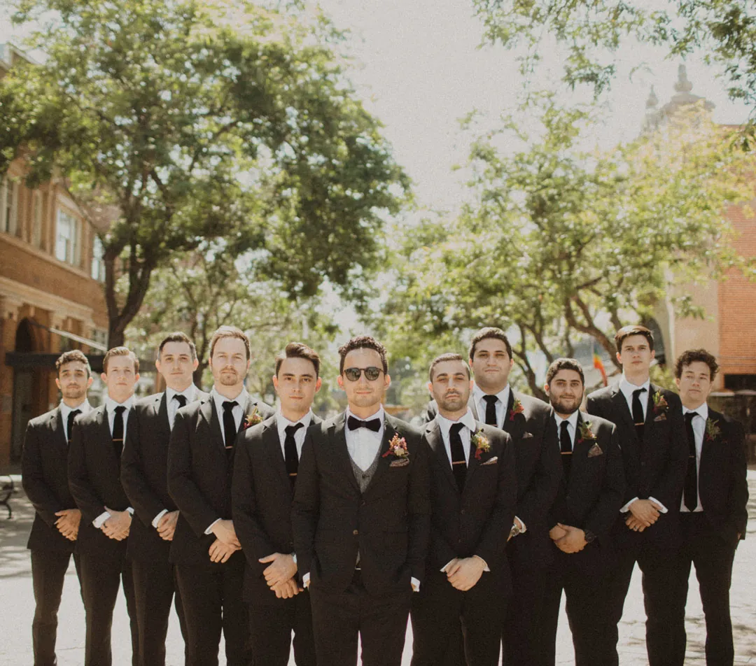 Groomsmen lined up outdoors beneath trees