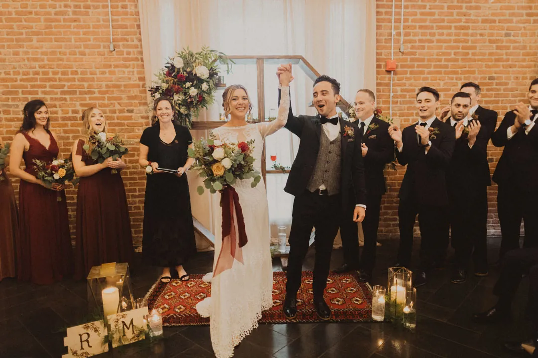 Newlyweds raising their arms with the wedding party behind them