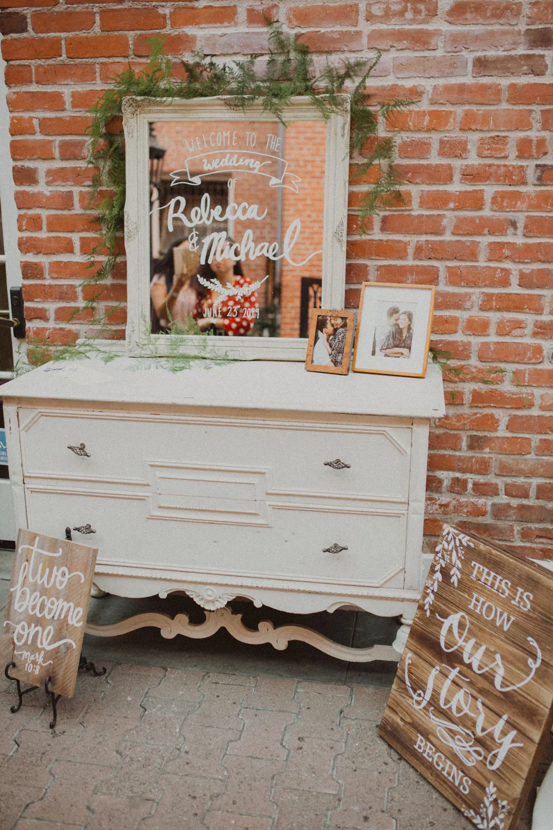 Framed wedding sign on a white dresser against a brick wall