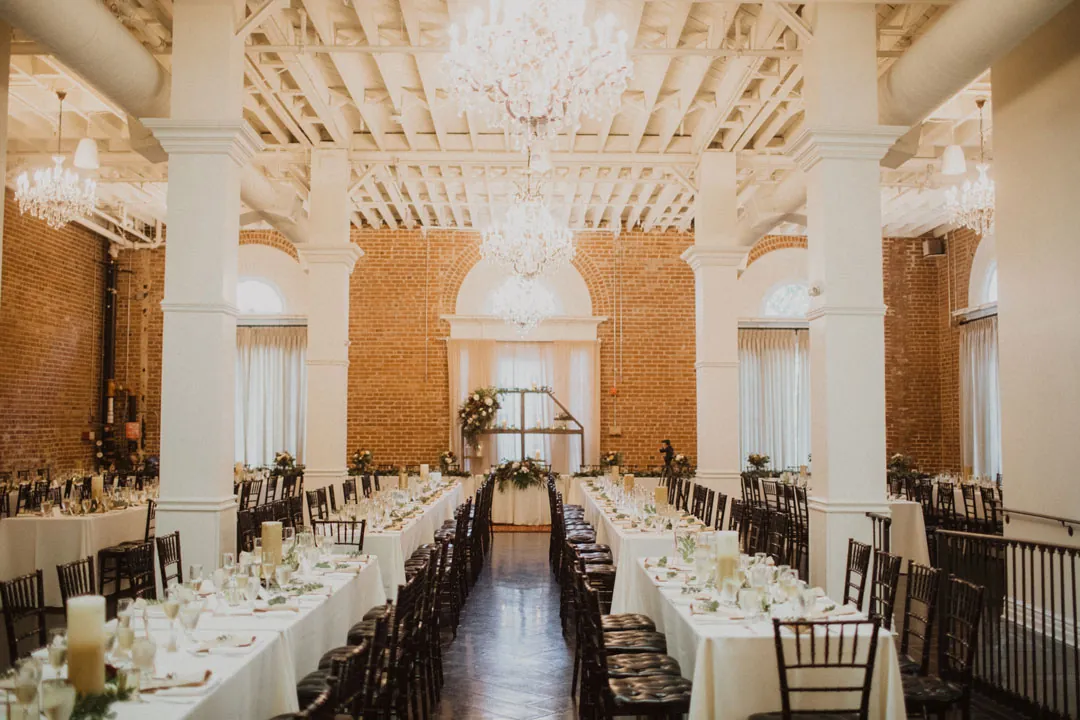 Reception tables arranged beneath chandeliers and exposed ceiling beams