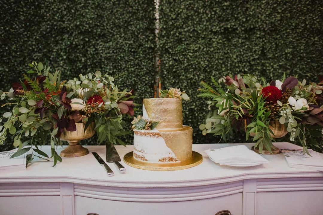Tiered wedding cake on a dresser against a greenery wall