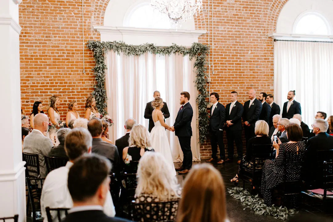 Wedding ceremony beneath chandeliers and white beams