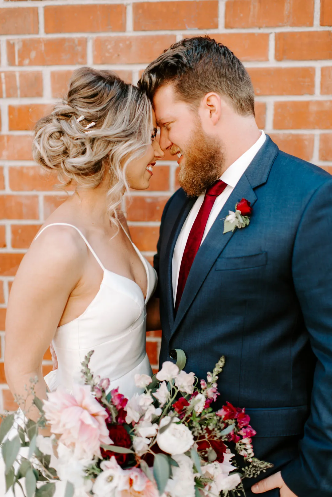 Bride and groom touching foreheads beside a brick wall