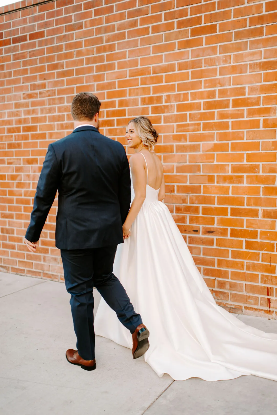 Bride and groom walking beside a brick wall