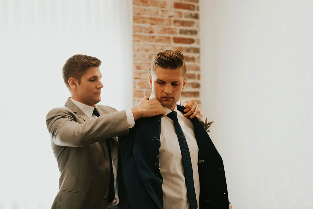 Attendant adjusts the collar of a groom's jacket.