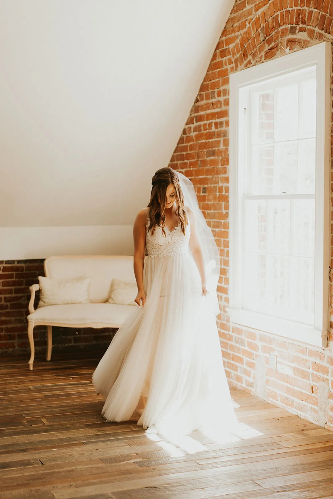 Bride stands beside a window with her train spread out.