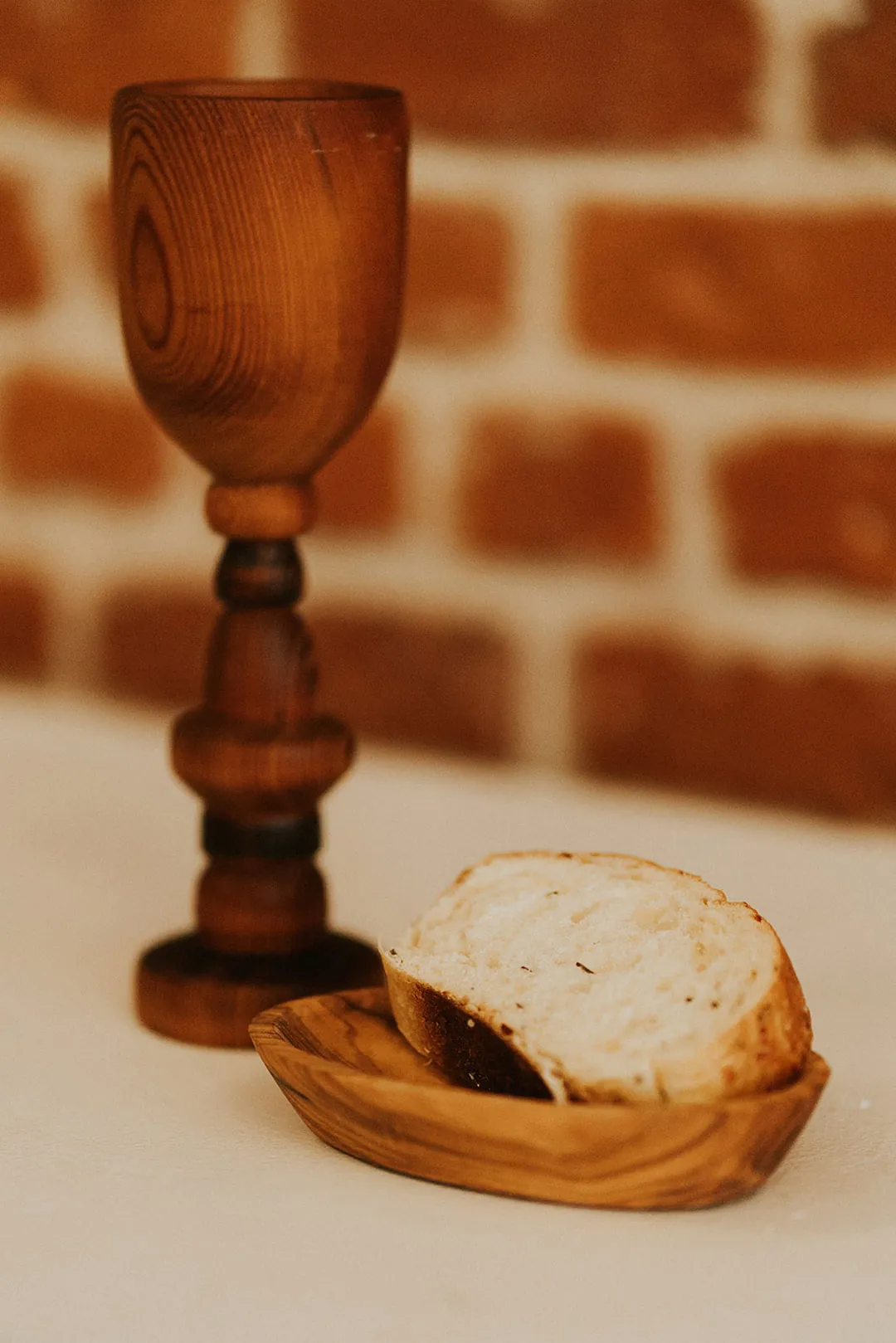 Wooden goblet beside sliced bread on a white cloth.