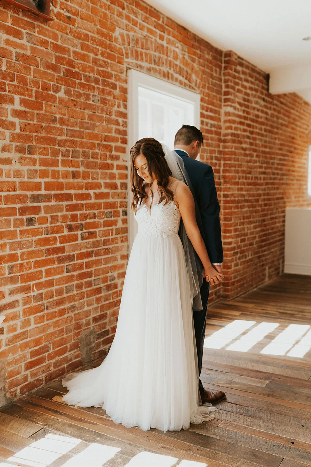 Couple stand back to back beside a brick wall.
