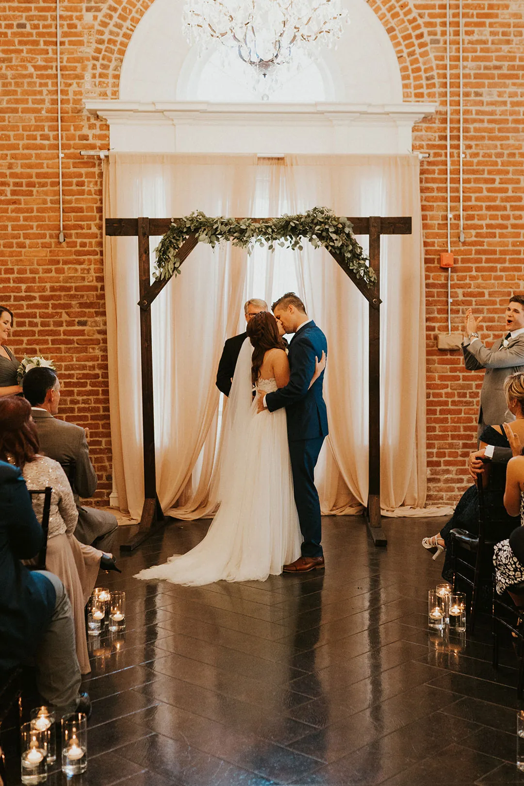 Newlyweds kiss before a geometric ceremony backdrop.