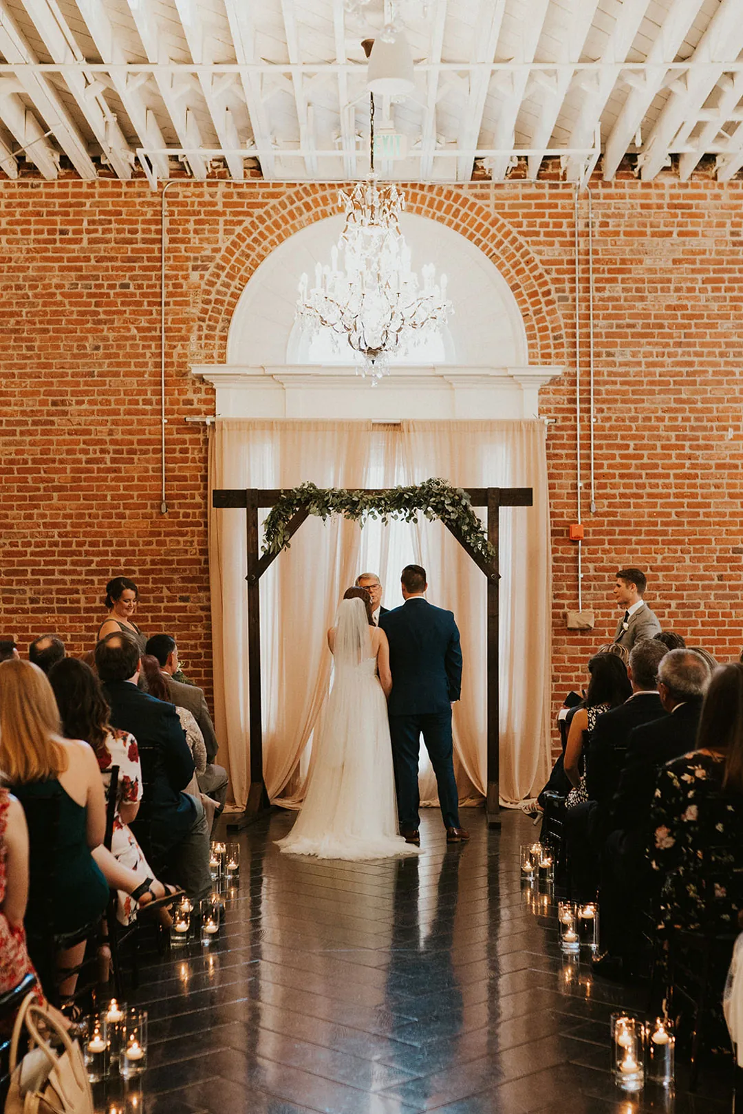 Guests face the couple during a ballroom ceremony.