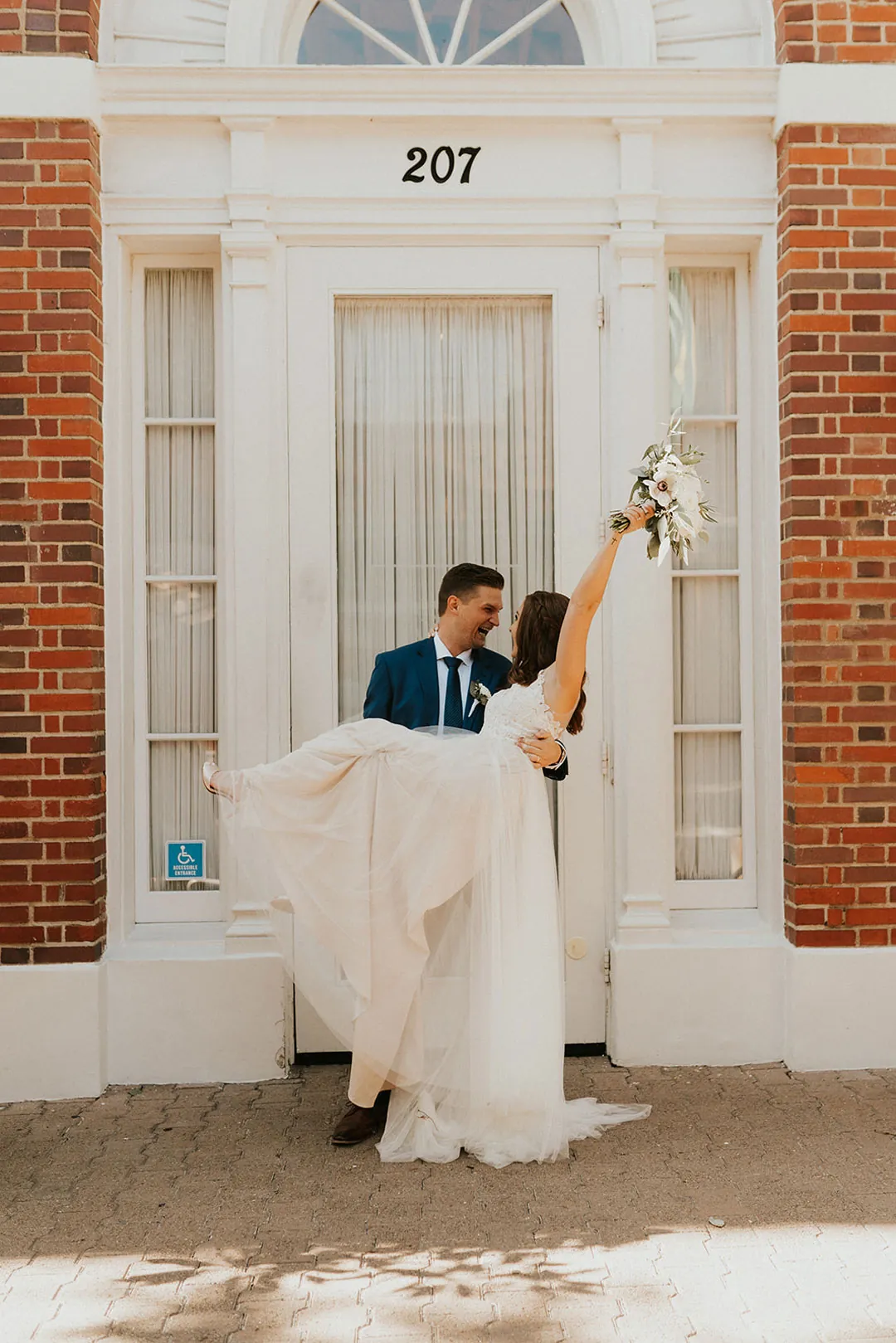 Groom lifts the bride beside an exterior doorway.