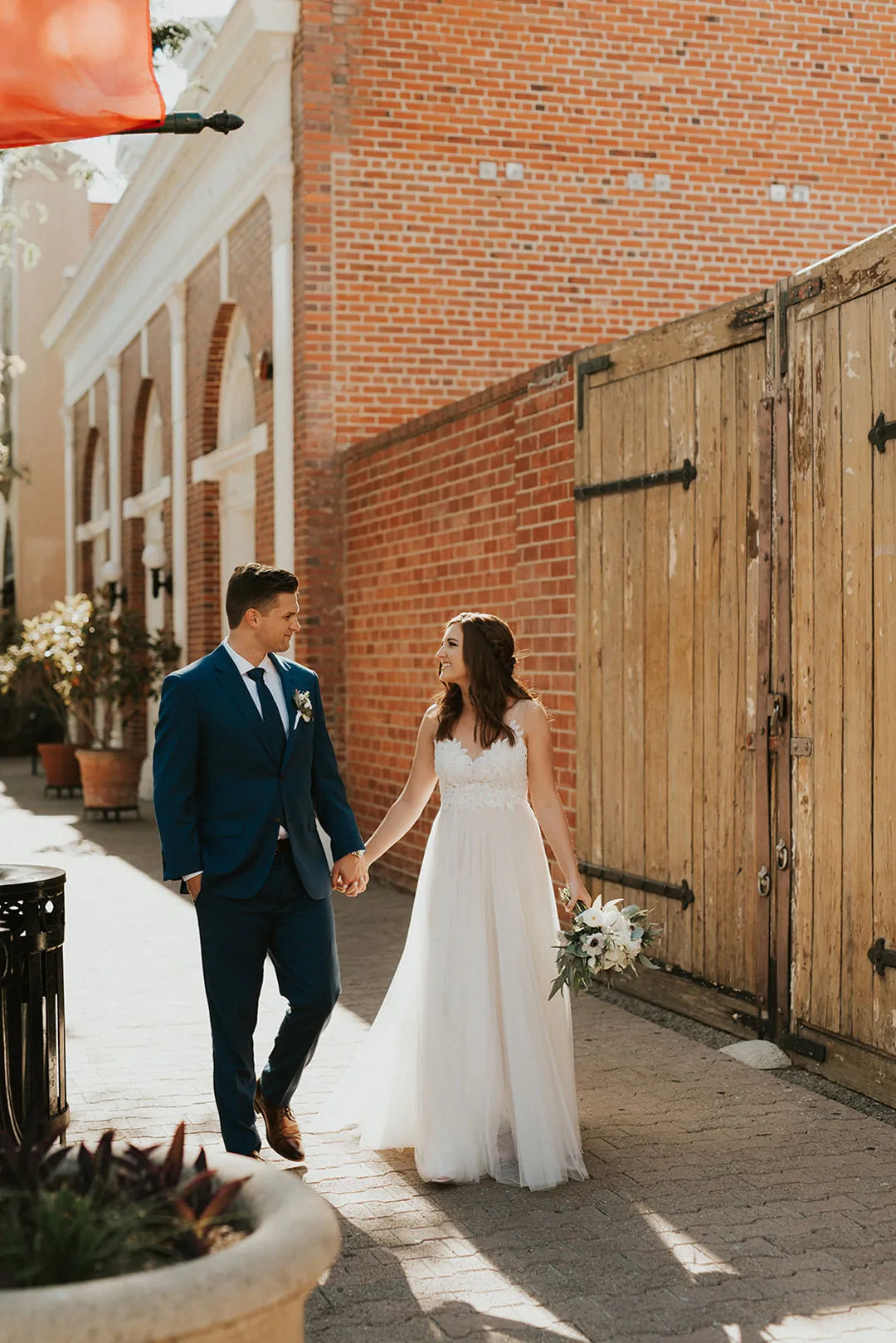 Newlyweds walk along a brick lined city street.