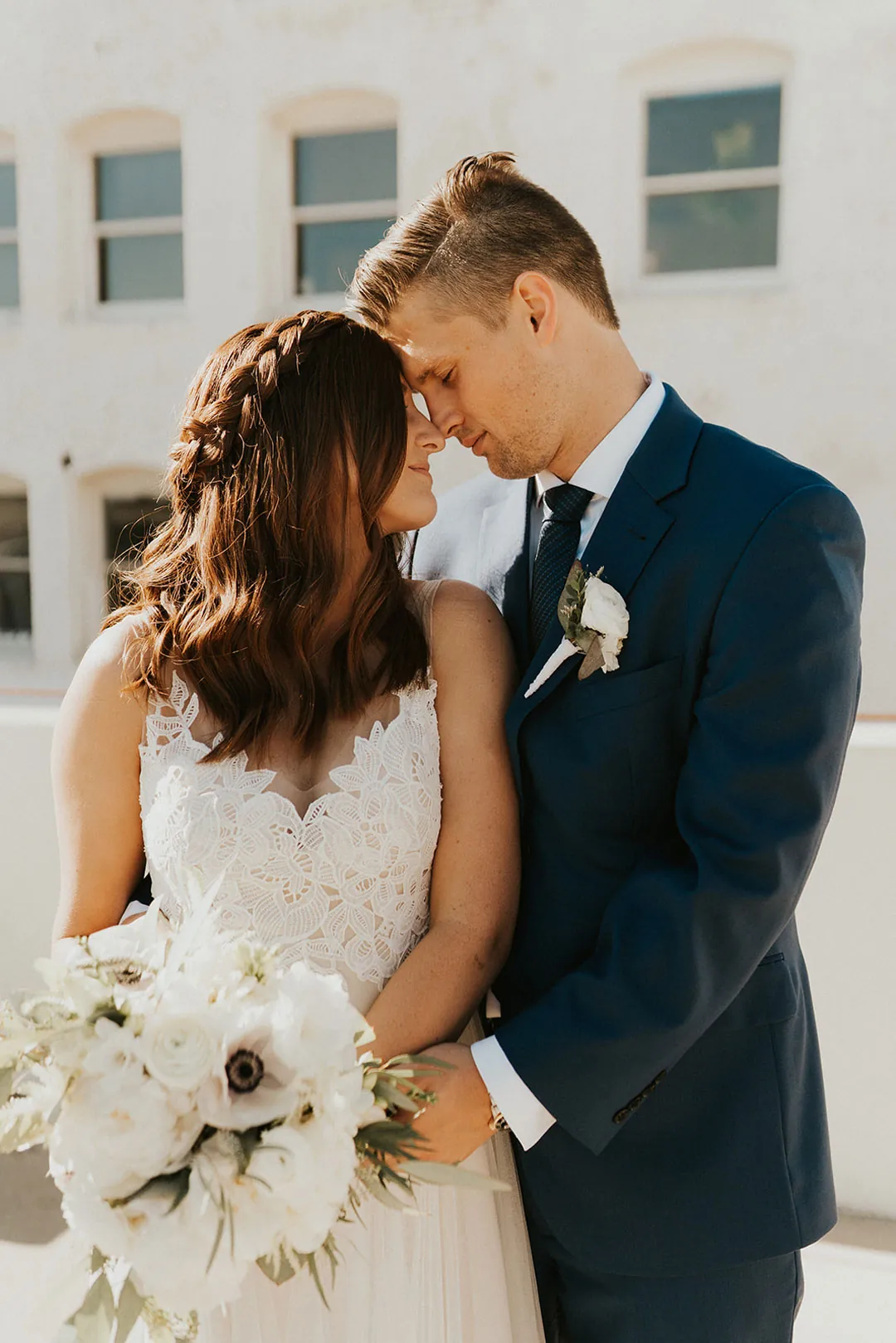 Groom kisses the bride's forehead outdoors.