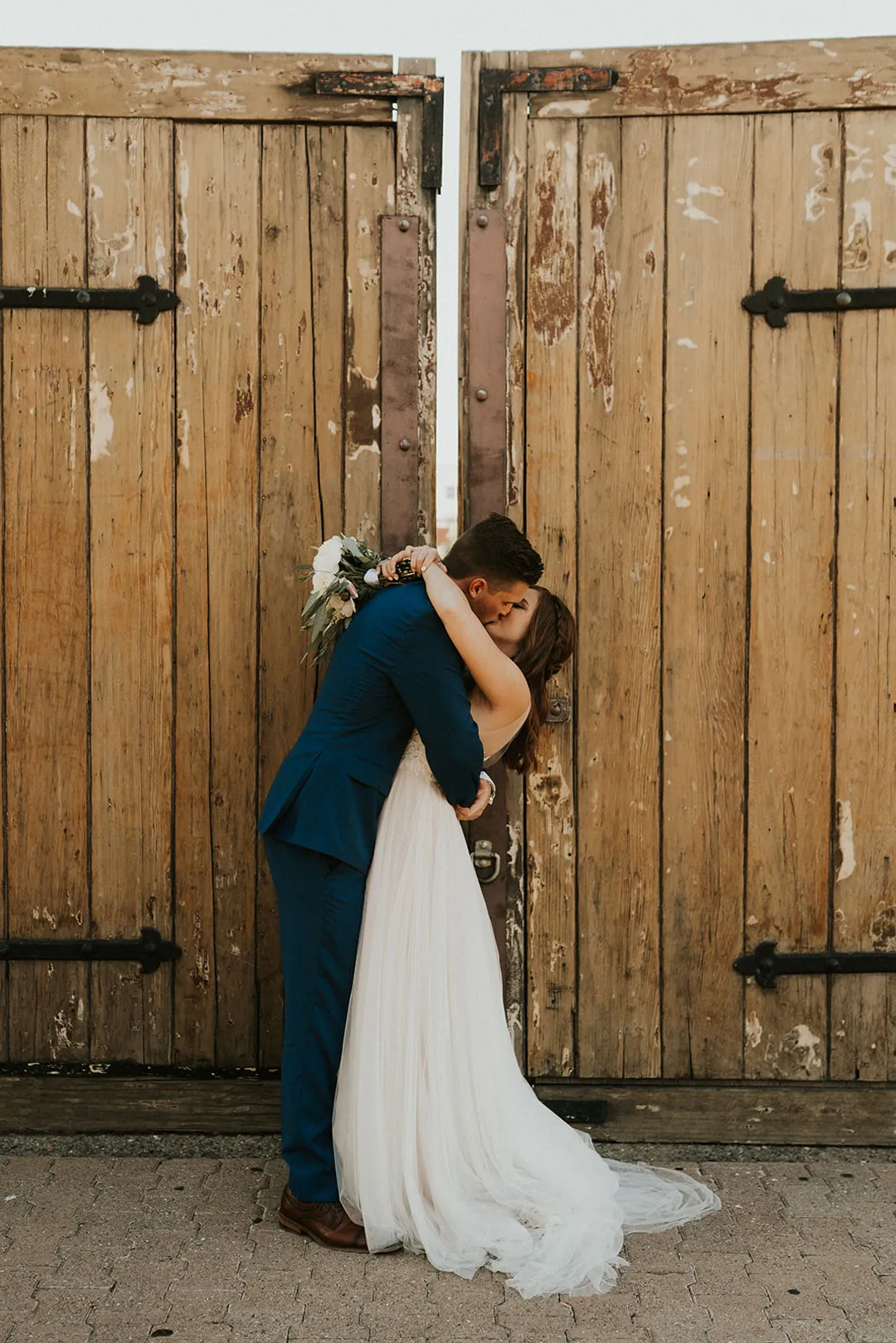 Newlyweds kiss beside a large wooden doorway.