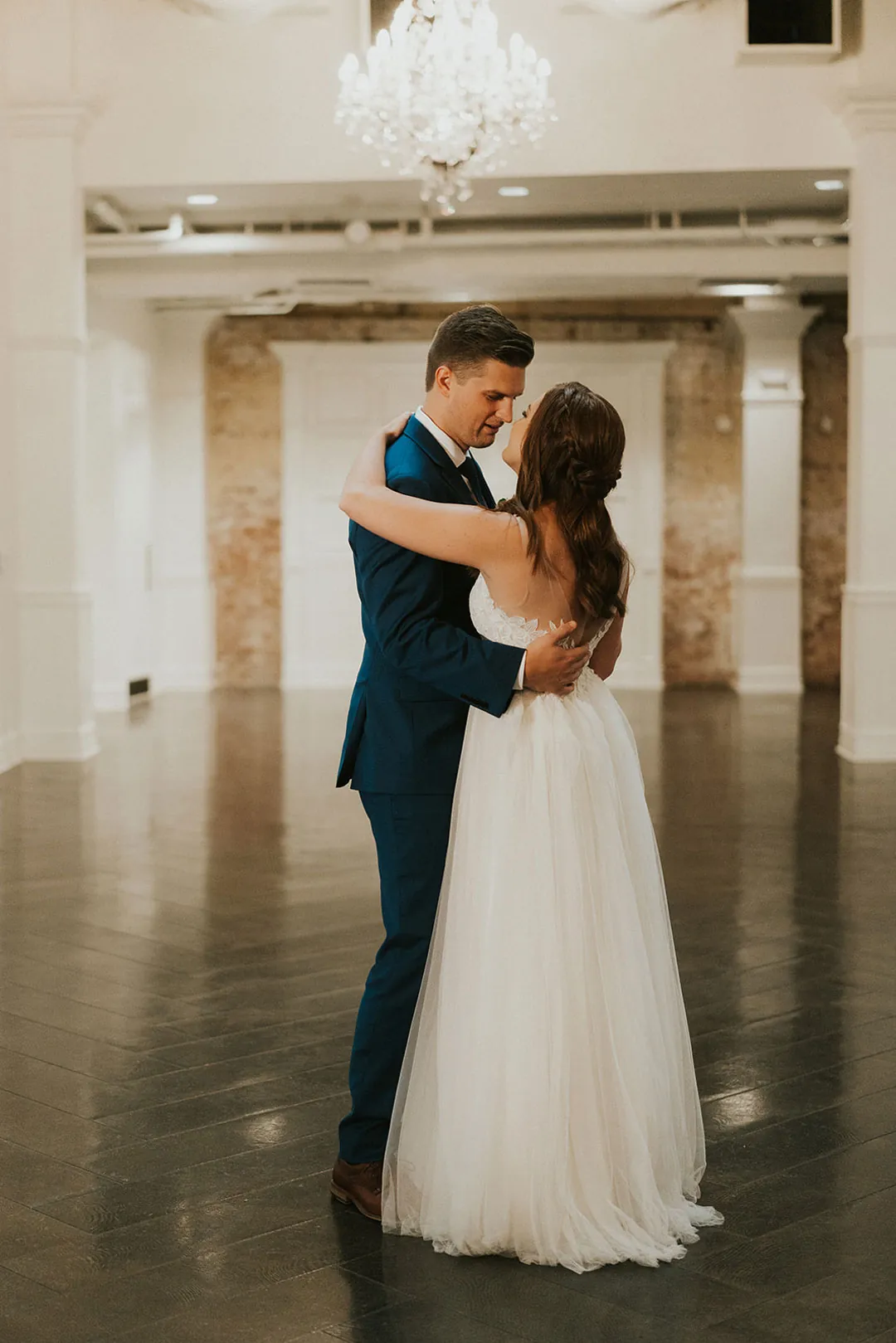 Newlyweds dance closely together on the ballroom floor.