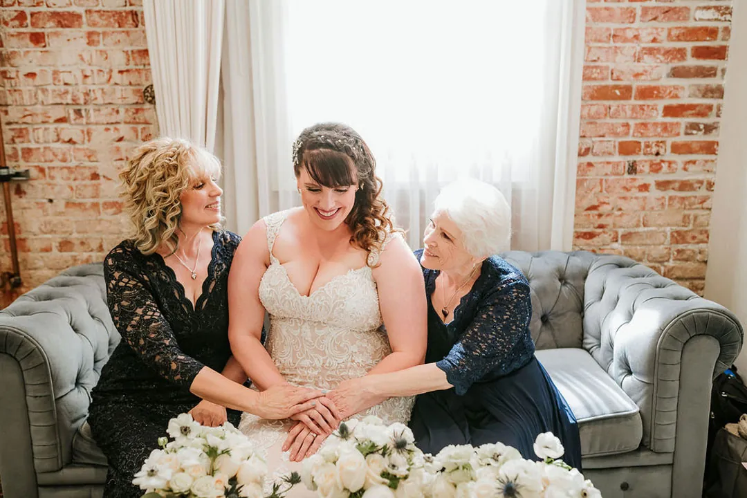 Bride sits between two guests on a gray sofa.