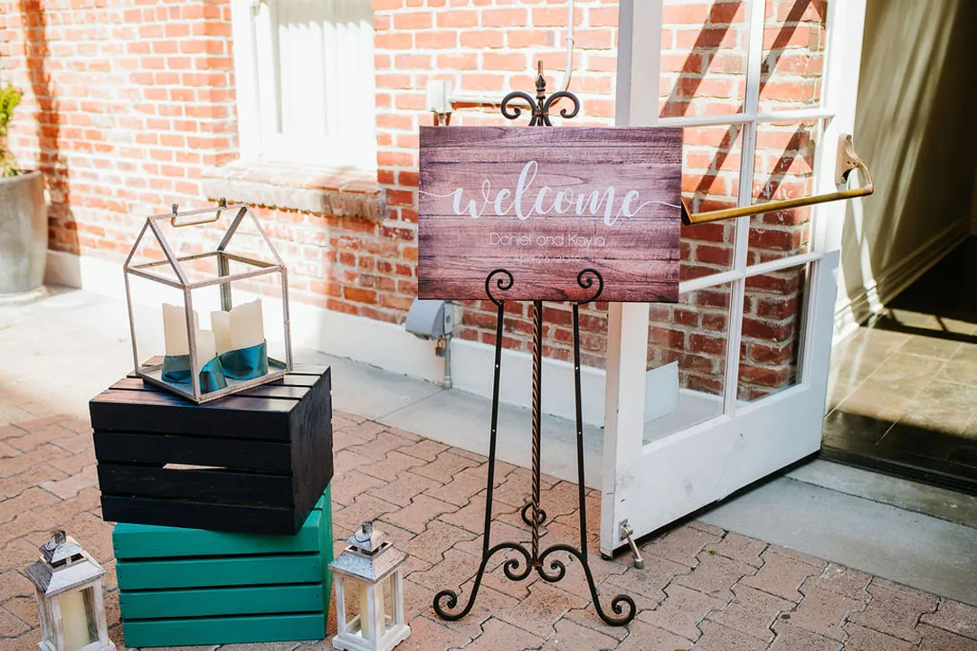 Wedding welcome sign beside stacked suitcases and a lantern.
