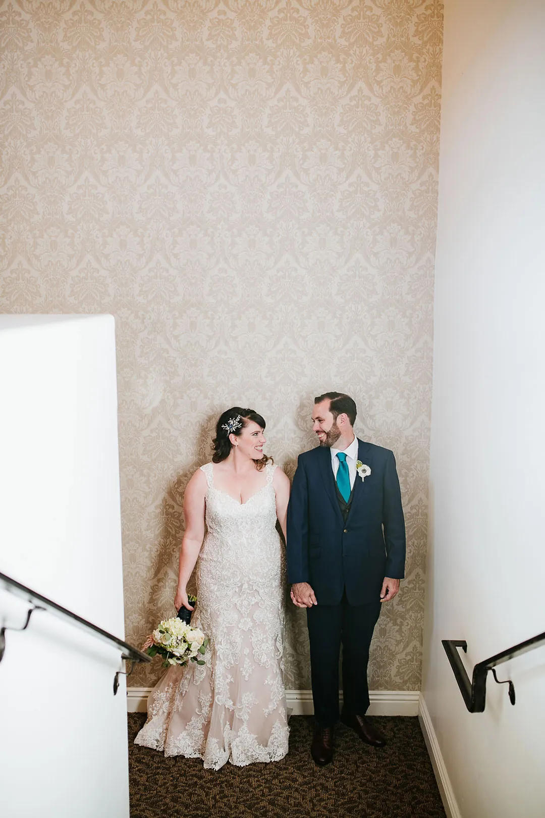 Couple stand together on an indoor stair landing.