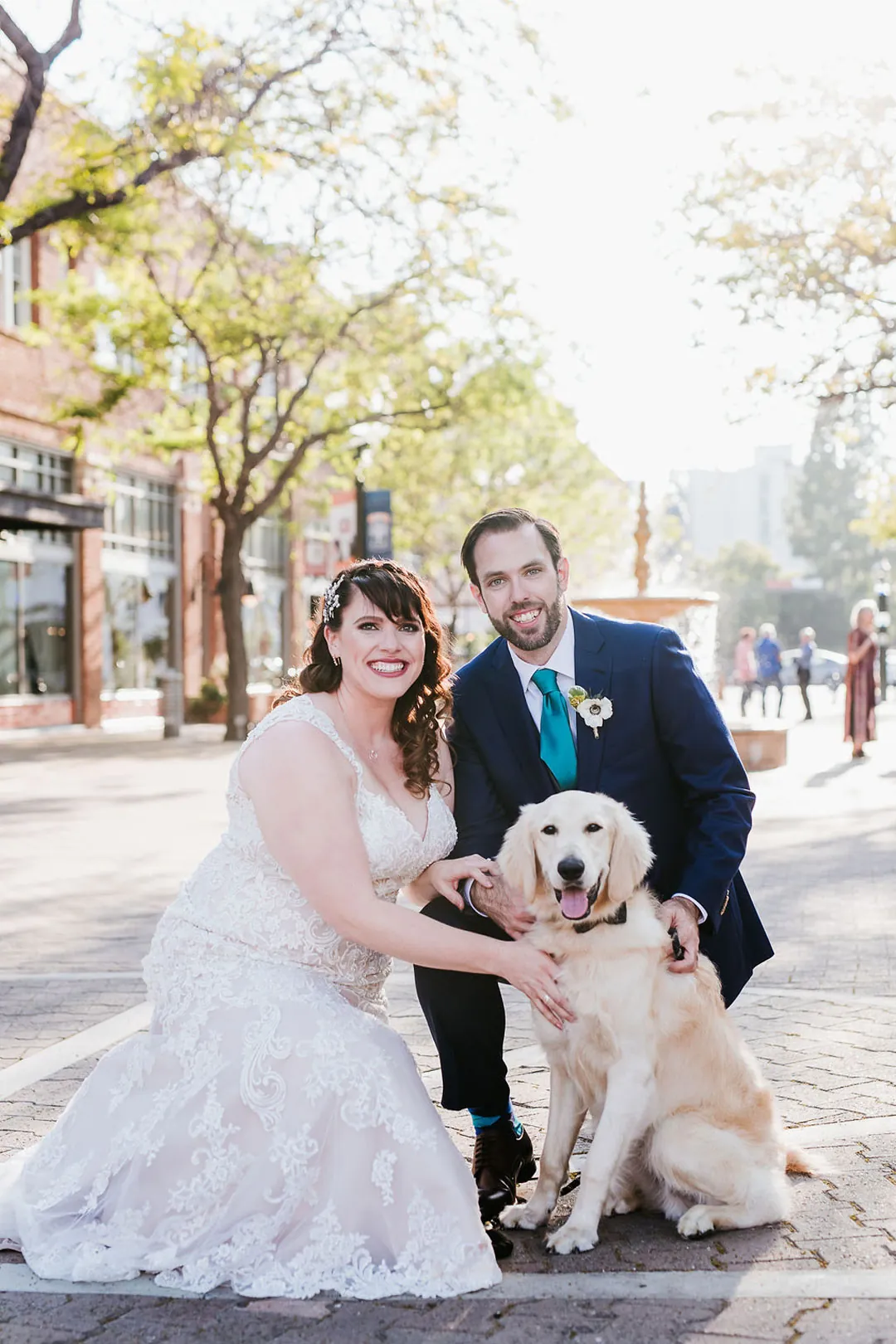 Newlyweds pose outdoors with a small dog.