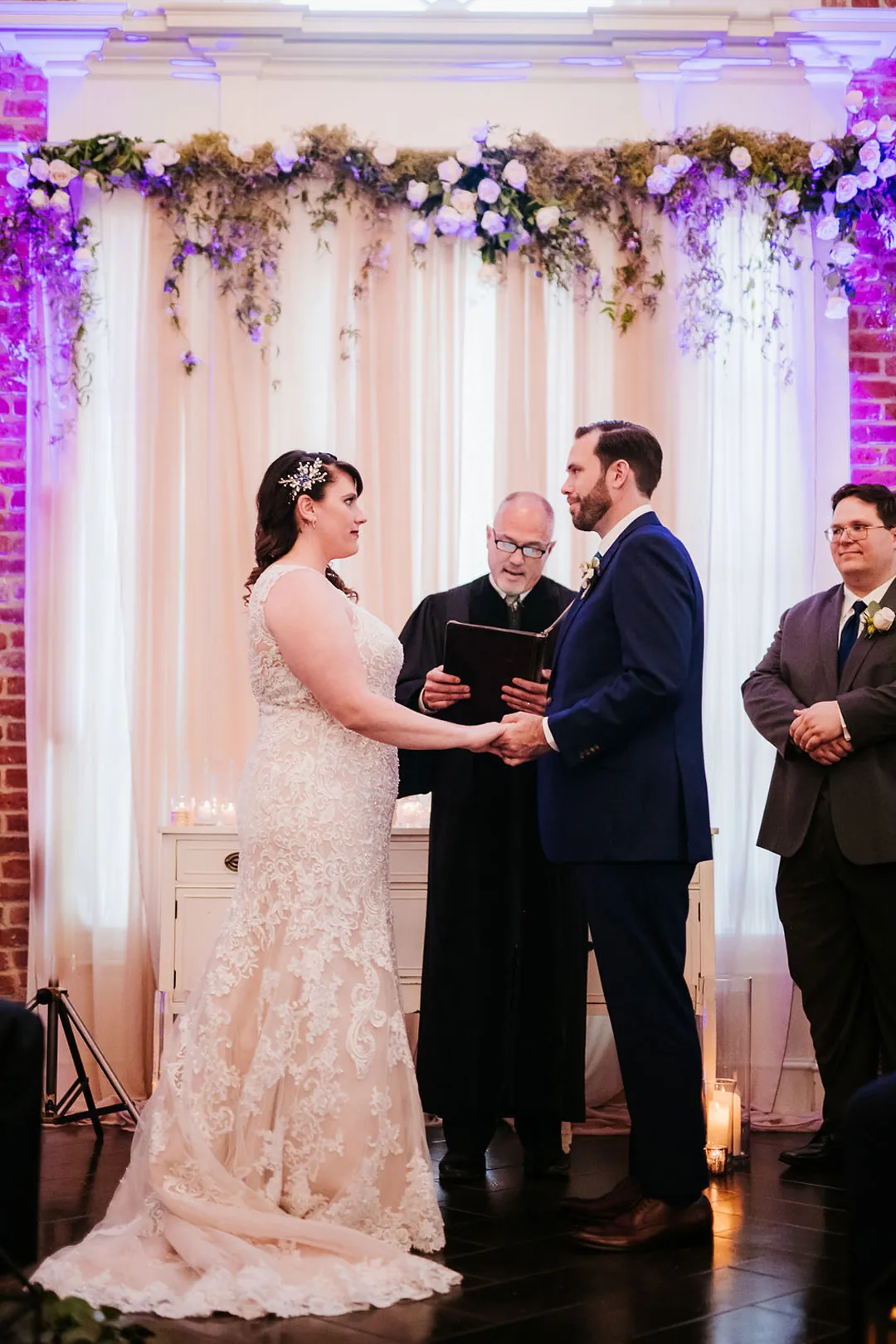Couple hold hands beside the officiant at their ceremony.