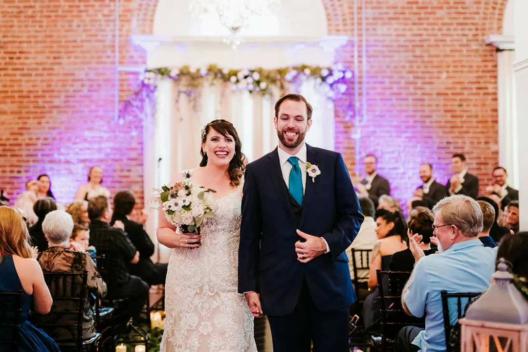 Newlyweds walk down the aisle between seated guests.