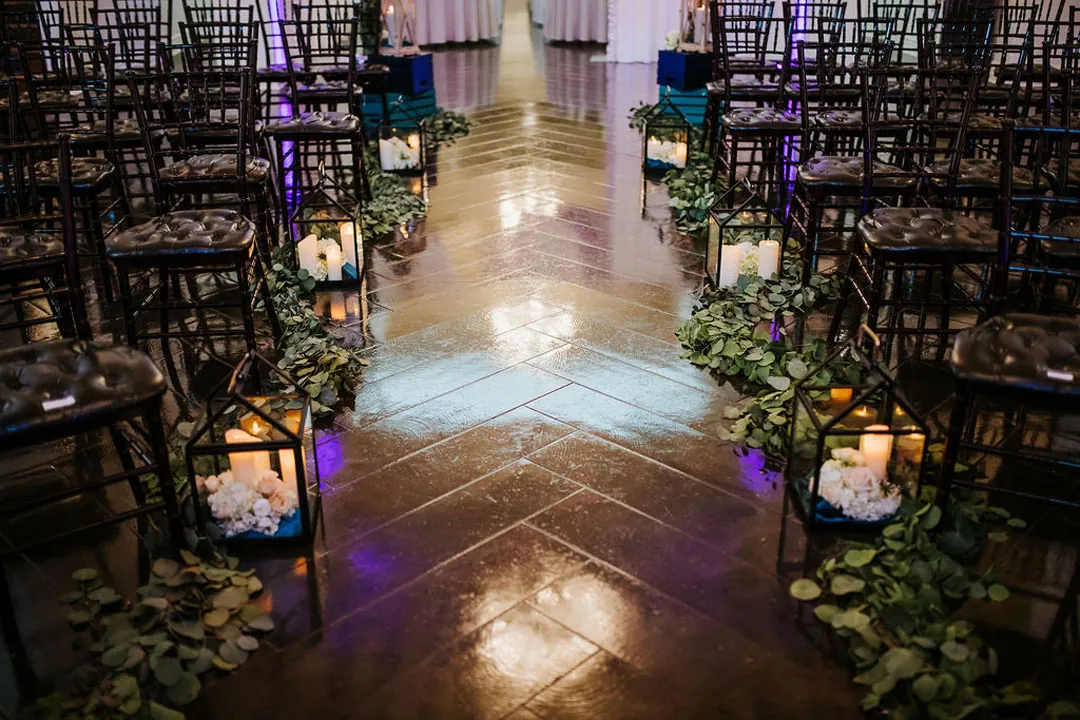 Greenery and lanterns line the ballroom ceremony aisle.
