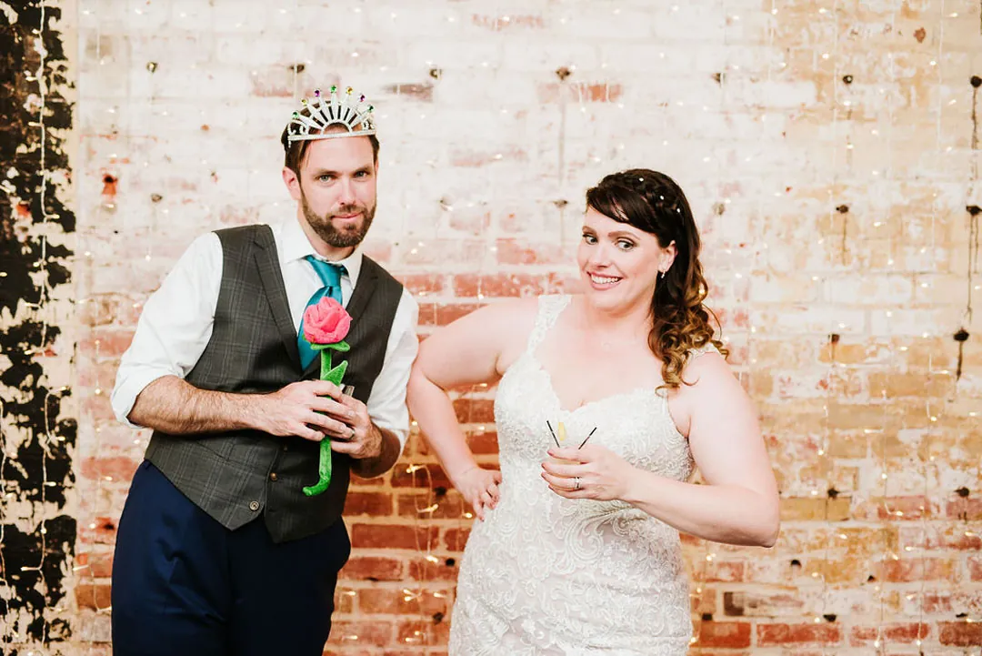 Couple pose playfully holding large colorful paper flowers.